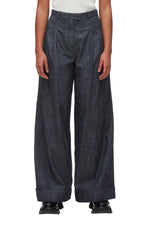 A person wears the 3.1 Phillip Lim Denim Double Pleat Wide Leg Pant in dark denim, featuring cuffed hems, paired with black shoes. The photo captures a modern yet classic silhouette from shoulders to feet against a white background.