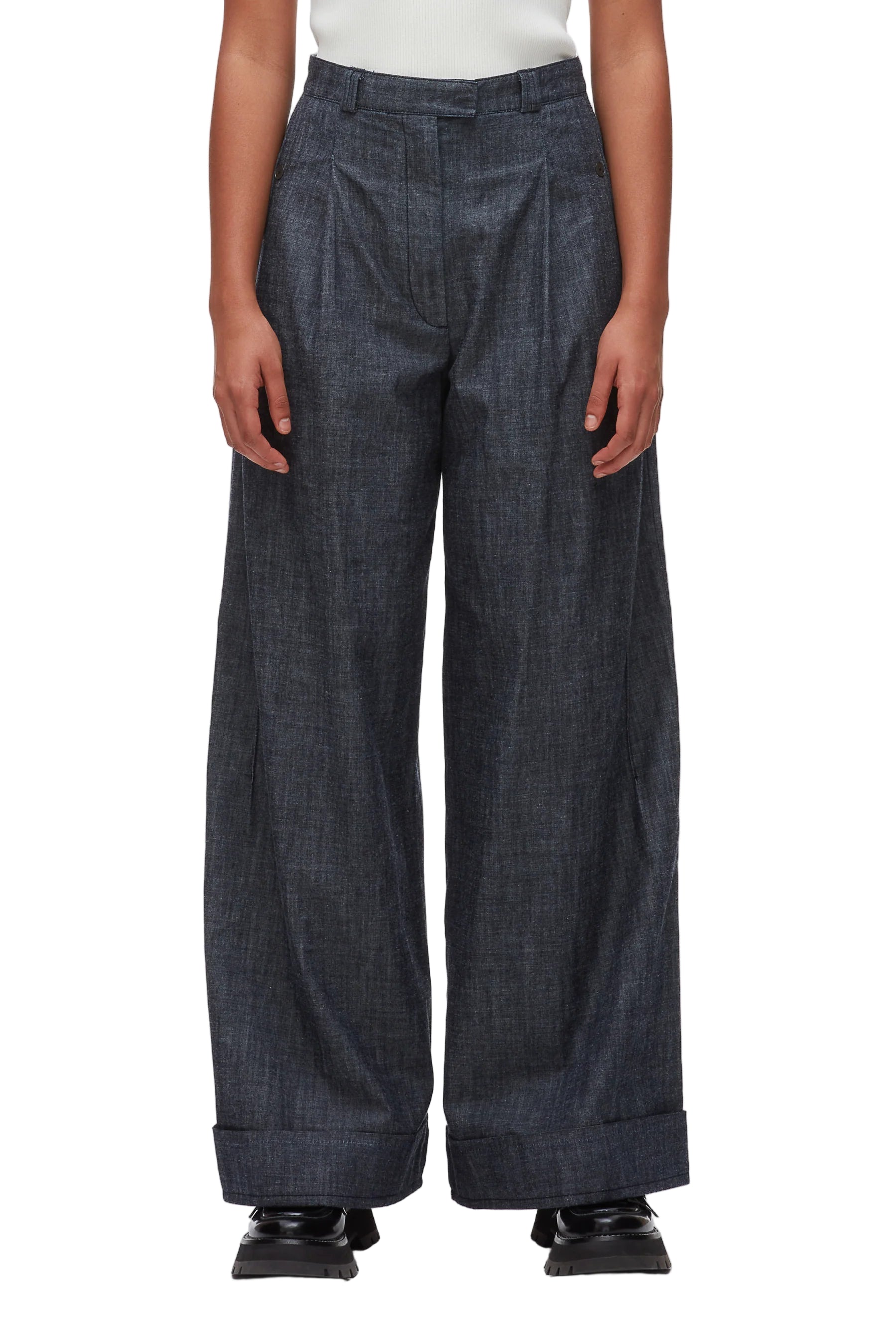 A person wears the 3.1 Phillip Lim Denim Double Pleat Wide Leg Pant in dark denim, featuring cuffed hems, paired with black shoes. The photo captures a modern yet classic silhouette from shoulders to feet against a white background.