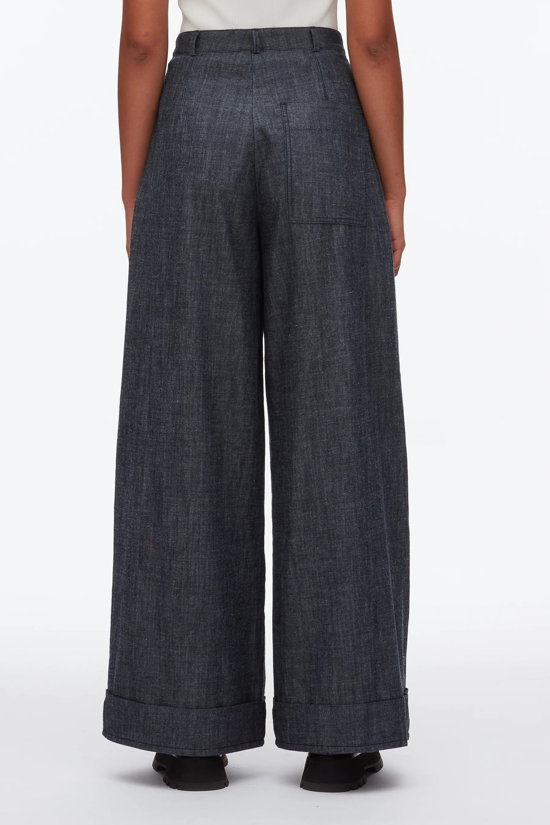A person is seen from the back wearing the 3.1 Phillip Lim Denim Double Pleat Wide Leg Pant, featuring high-waisted, wide-leg styling with cuffed hems, set against a plain white background.