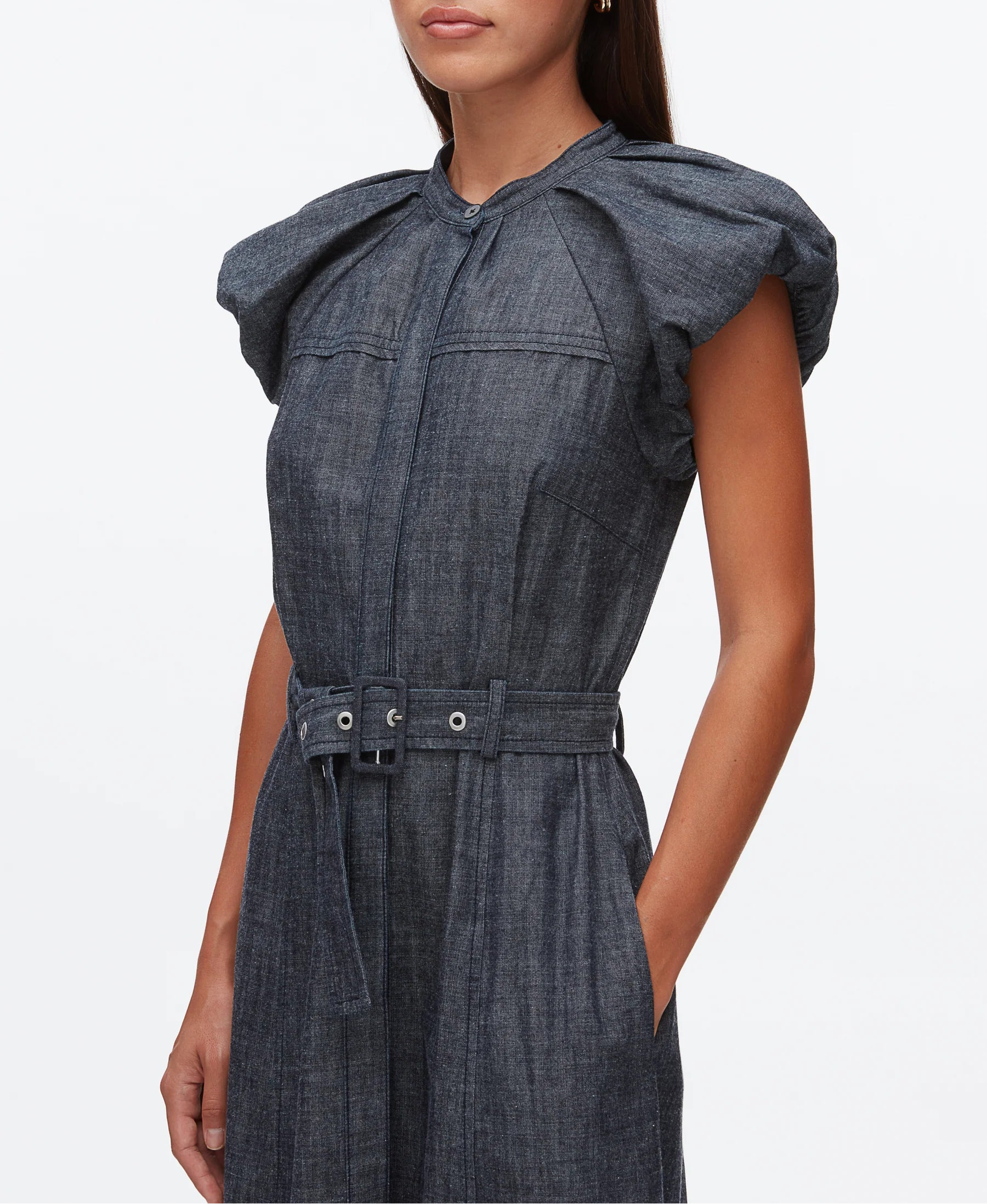 A woman wears the 3.1 Phillip Lim Denim Puff Sleeve Dress, a belted midi with short puff sleeves, pleated shoulders, and a high neckline.