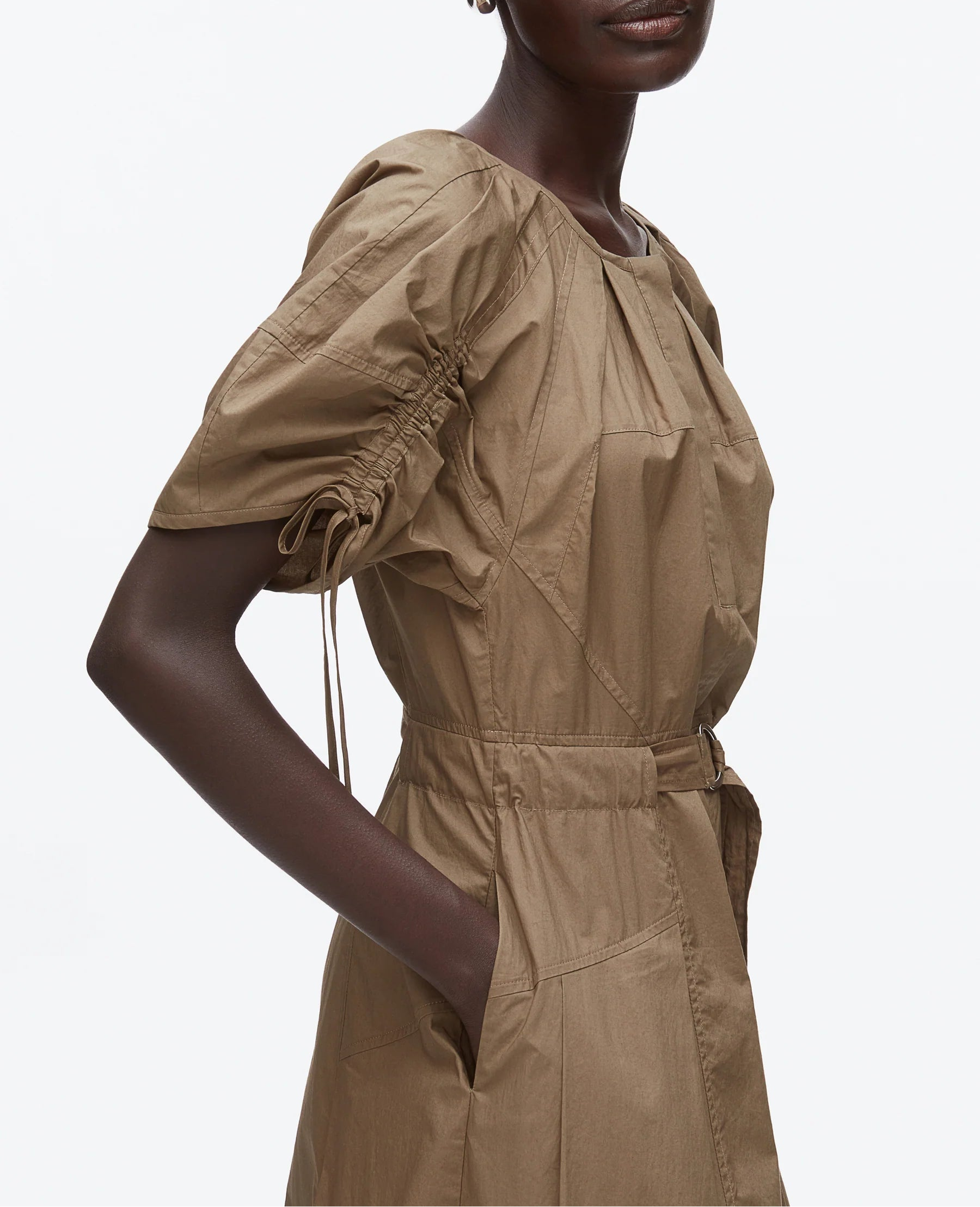 A person wears the 3.1 Phillip Lim Ruched Sleeve Midi Dress, a belted, short-sleeve, light brown cotton poplin dress with gathered details and hands in pockets, against a plain white background.