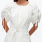 A woman models the 3.1 Phillip Lim Ruched Sleeve Midi Dress, featuring white cotton poplin, puffed short sleeves, ruched details, a round neckline, and a D-ring belt, set against a plain background.