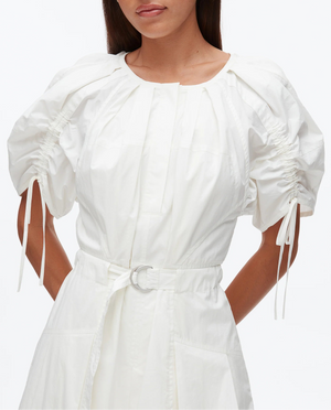 A woman models the 3.1 Phillip Lim Ruched Sleeve Midi Dress, featuring white cotton poplin, puffed short sleeves, ruched details, a round neckline, and a D-ring belt, set against a plain background.