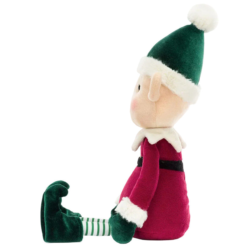 Profile view of a Jellycat Eldo Elf plush wearing a green and red outfit with a white-trimmed pointed hat and striped stockings.