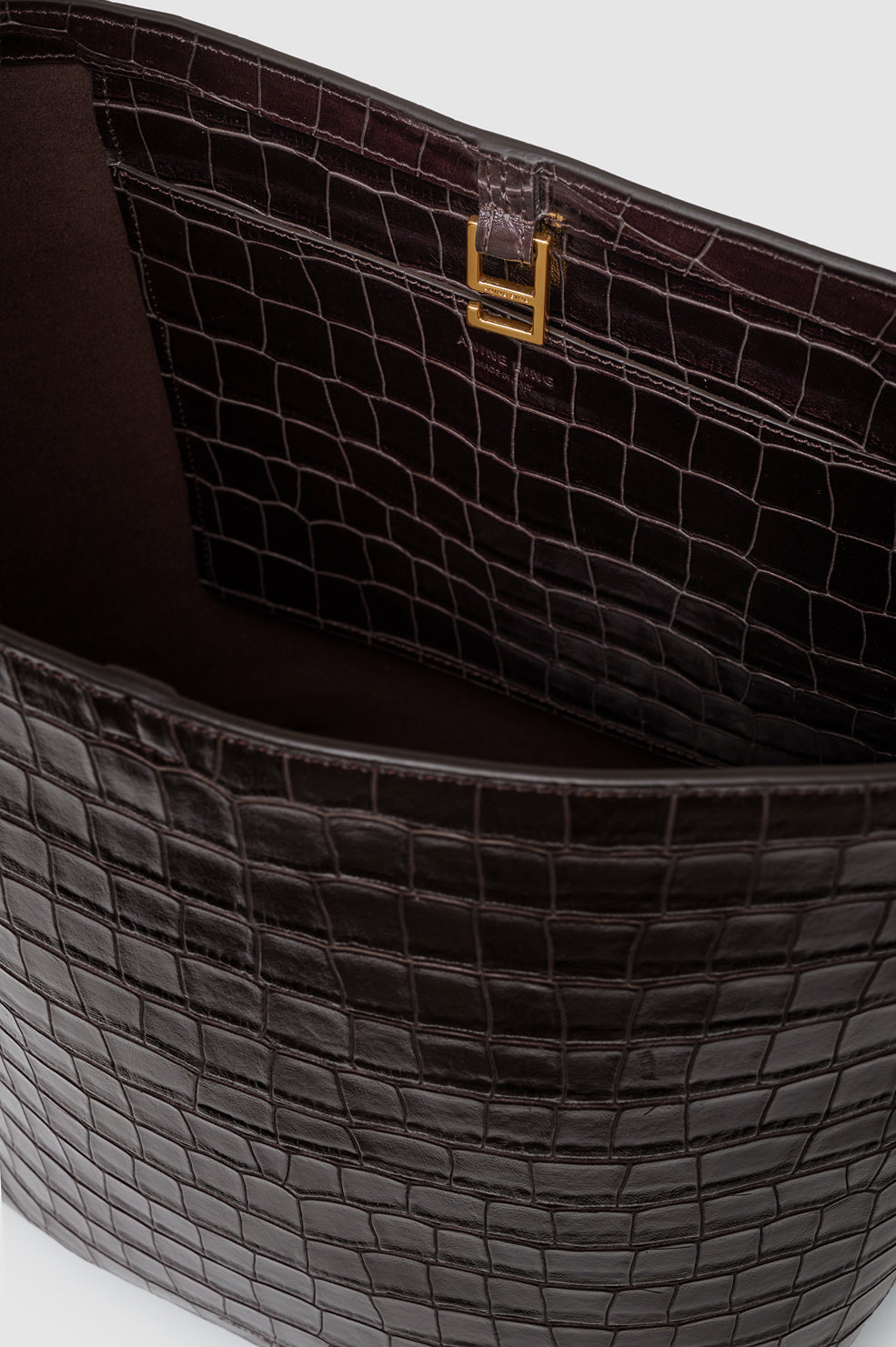 Interior view of an Anine Bing Elly Bucket Embossed Bag in dark brown crocodile-embossed leather with gold-tone hardware at the closure.
