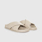 The Emi Slides by Anine Bing are beige flat sandals featuring padded cross-over straps and flat soles, shown on a plain light background.
