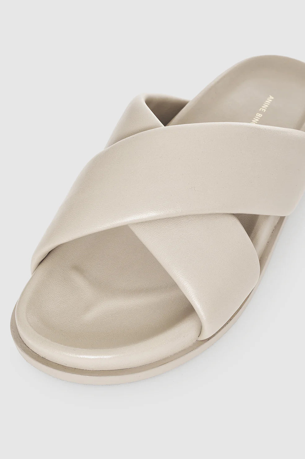 A close-up of the Anine Bing Emi Slides in olive lambskin leather, featuring wide padded cross-over straps and a flat sole, shown on a plain background.