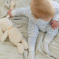 A baby in the Joy Street Baby Seaside Zip Onesie sits on a blanket beside a plush toy, reaching for its tail—capturing that sunny seaside vibe.