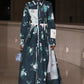 A model walks an indoor runway in the Erdem Long Sleeve Abstract Rose Shirt Dress, featuring a collared design with abstract rose print, and carries a small textured handbag.