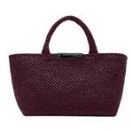 The Proenza Schouler East West Raffia Chelsea Tote is a structured handbag in dark burgundy with two handles and a black rectangular label on the front, effortlessly combining style and sophistication.