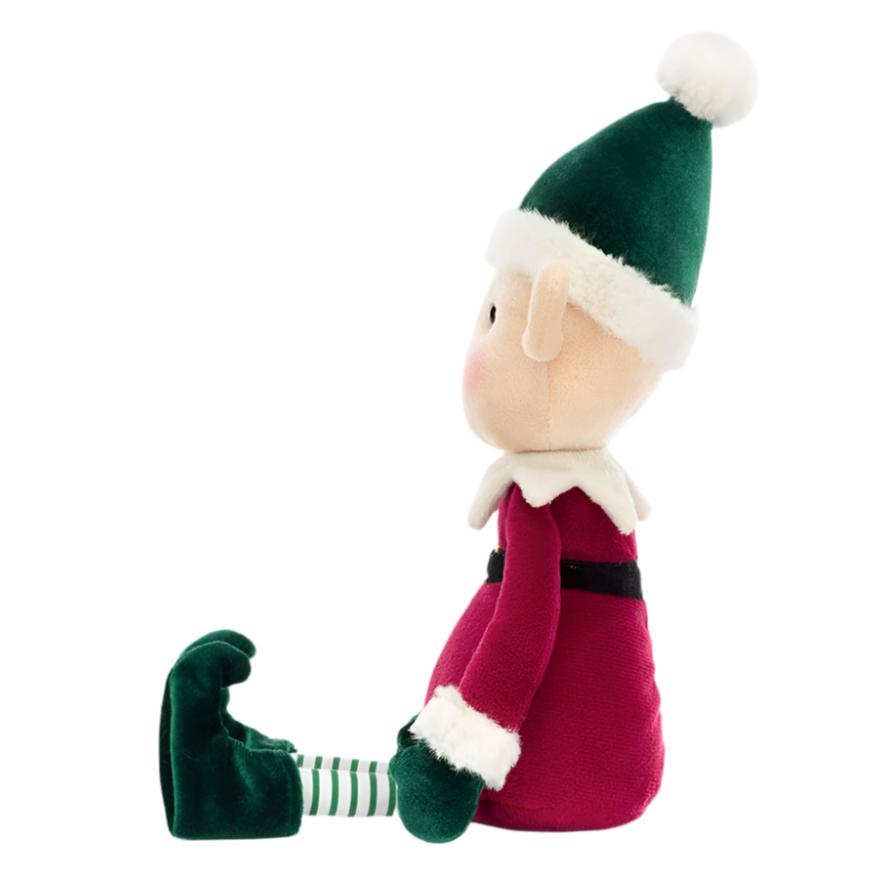 Side view of the plush Jellycat Eldo Elf doll from Jellycat, dressed in a festive red and green outfit. It sits upright with striped green and white leggings and a charming green hat, ready to spread Christmas cheer.