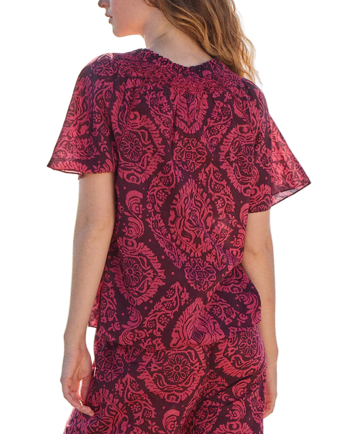 A woman is seen from the back wearing the Figue Elena Top—short-sleeve, magenta and pink with a smocked neckline—crafted from lightweight cotton voile, paired with matching pants, all set against a white background.