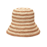 The Mar Y Sol Eleni Hat is a woven bucket sun hat with alternating beige and light brown horizontal stripes, shown on a white background. Its comfortable brim provides stylish sun protection for any outing.