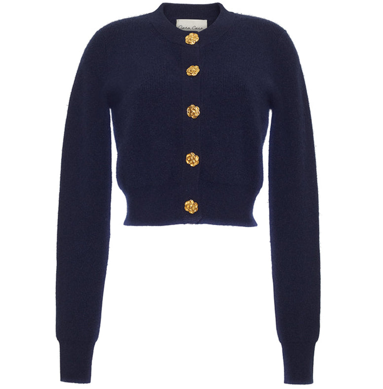 The Cara Cara Ellery Cardigan is a navy blue, crewneck sweater with long sleeves and gold floral buttons down the front, shown on a white background.
