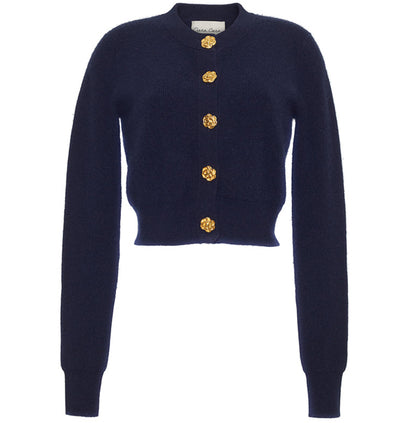 The Cara Cara Ellery Cardigan is a navy blue, crewneck sweater with long sleeves and gold floral buttons down the front, shown on a white background.