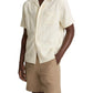 A person wears the vince Embroidered Floral Shortsleeve Cabana Shirt, cream-colored with a subtle floral pattern, paired with tan shorts and standing with one hand in their pocket.