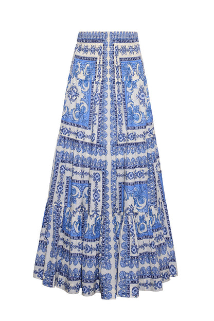 The Cara Cara Emilia Skirt is a long, voluminous piece with a blue and white tile pattern featuring floral and decorative details, plus two front pockets.