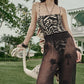A woman outdoors in a wide-brimmed hat and the Whispering Tides One Piece by Johanna Ortiz leans on a white flamingo statue.