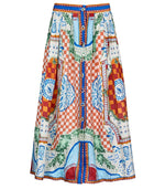 The Eva Skirt by Hunter Bell NYC is a long, high-waisted skirt in a linen-rayon blend, featuring a vibrant patchwork pattern with red and white checks, blue and green accents, and decorative motifs.