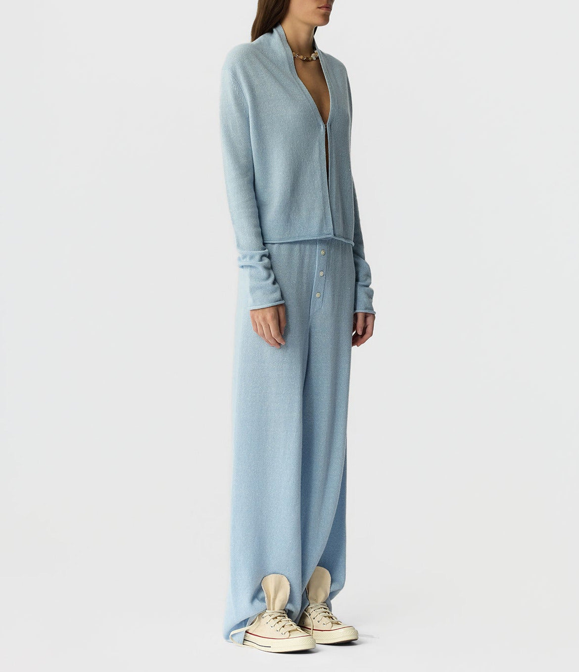 A person stands against a plain background wearing a light blue zip-up sweater, beige sneakers, and the Guest in Residence Everywear Cashmere Pant.