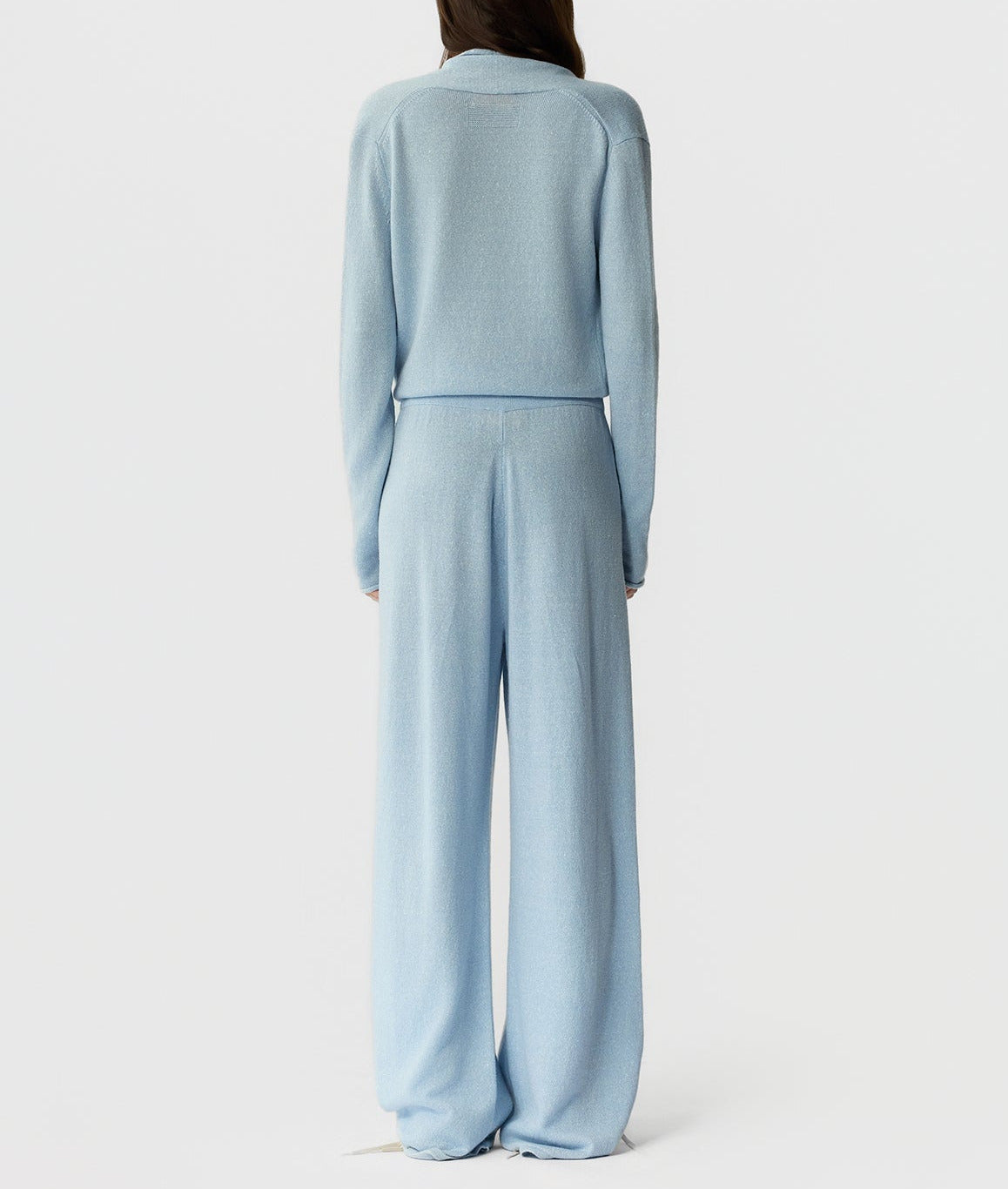 A person stands with their back to the camera, wearing a light blue long-sleeve top and matching Guest in Residence Everywear Cashmere Pants against a plain white background.