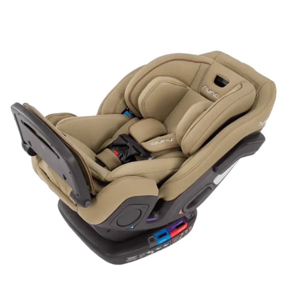 A beige Nuna EXEC car seat with a slip cover and second insert, featuring cushioned pads and a safety harness. The base includes colorful indicators, a multi-functioning adjustable leg rest, and an Aeroflex side impact protection system for enhanced safety.