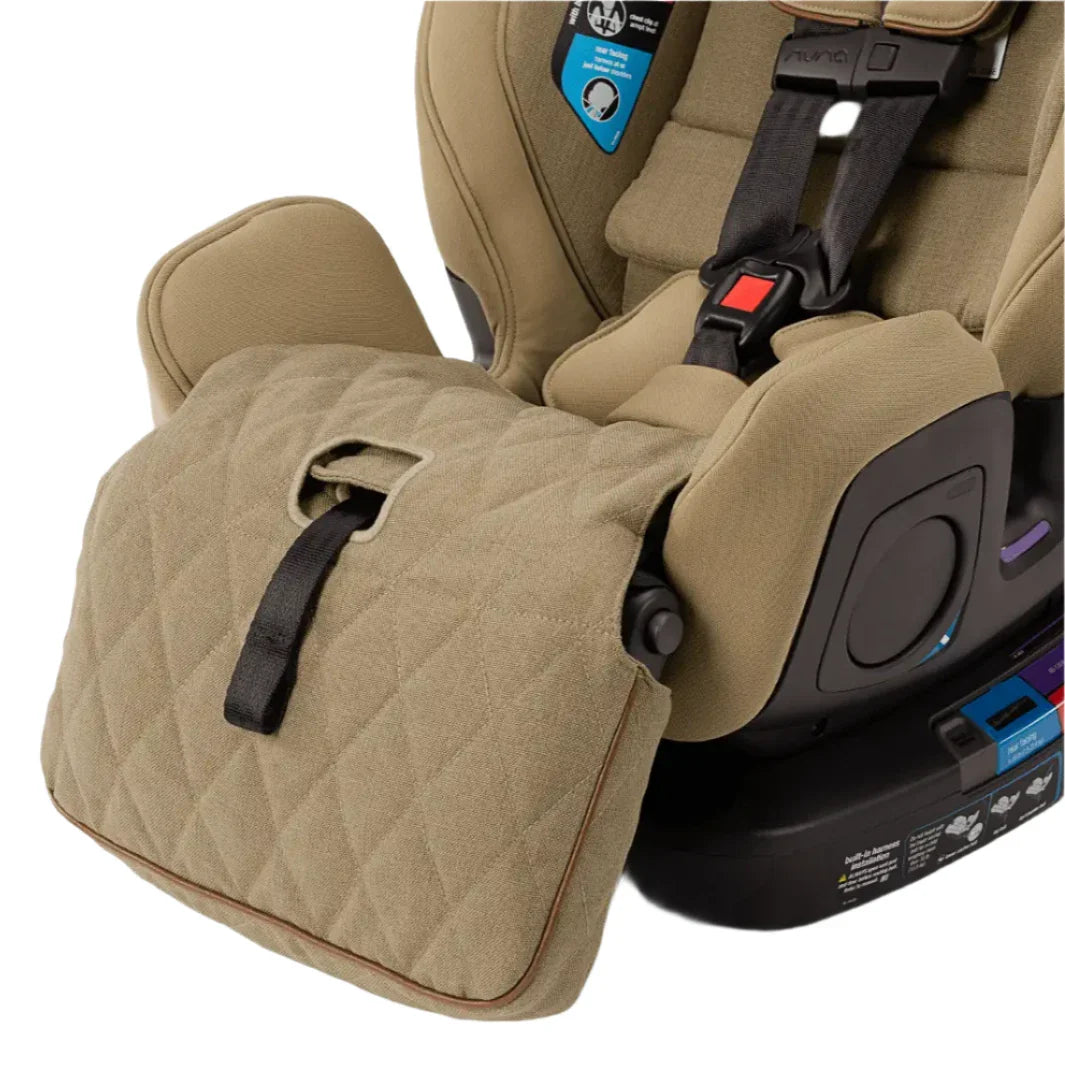 Close-up of the Nuna EXEC with Slip Cover and 2nd Insert, a beige premium car seat by Nuna featuring a diamond-patterned cover, harness straps, safety labels on the side, and an adjustable leg rest for multi-functional comfort.