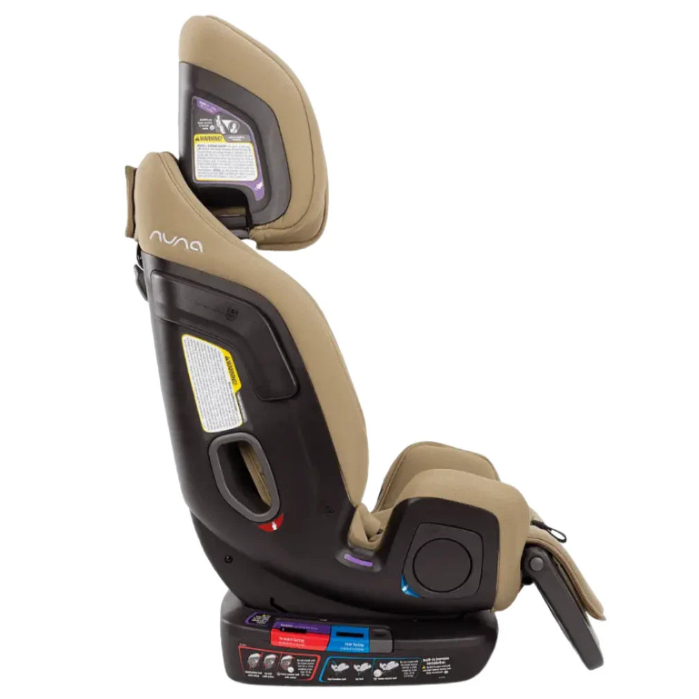 Side profile view of the Nuna EXEC with Slip Cover and 2nd Insert, a black and tan premium child's car seat by Nuna, featuring safety labels, an Aeroflex side impact protection system, and a multi-functioning adjustable leg rest.