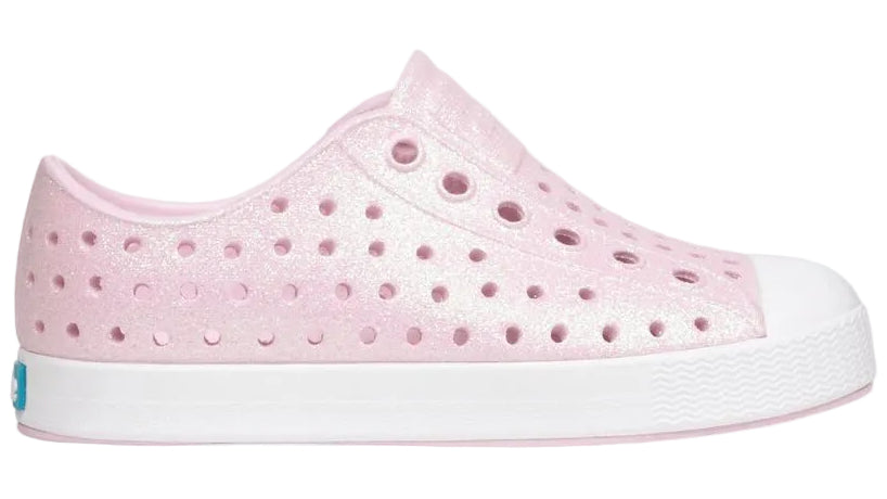 Introducing the Kids’ Jefferson Bio-Bling™ by Native Shoes—a pink, side-view slip-on sneaker featuring a white sole, perforated design, and shimmering biodegradable glitter. Made from lightweight EVA, these water-friendly shoes deliver eco-conscious sparkle and all-day comfort.