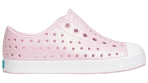 Introducing the Kids’ Jefferson Bio-Bling™ by Native Shoes—a pink, side-view slip-on sneaker featuring a white sole, perforated design, and shimmering biodegradable glitter. Made from lightweight EVA, these water-friendly shoes deliver eco-conscious sparkle and all-day comfort.