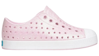 Introducing the Kids’ Jefferson Bio-Bling™ by Native Shoes—a pink, side-view slip-on sneaker featuring a white sole, perforated design, and shimmering biodegradable glitter. Made from lightweight EVA, these water-friendly shoes deliver eco-conscious sparkle and all-day comfort.