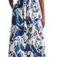 A person wearing an Altuzarra Altuzarra Paulina Dress, a long blue, white, and brown equestrian print dress with kimono-style sleeves, cinched at the waist with a matching belt, and black boots.