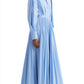 Person standing in an Altuzarra Binoche Dress by Altuzarra, a light blue, long-sleeved dress with balloon sleeves and an elasticated back, featuring a pleated skirt and paired with black pointed shoes, against a plain white background.