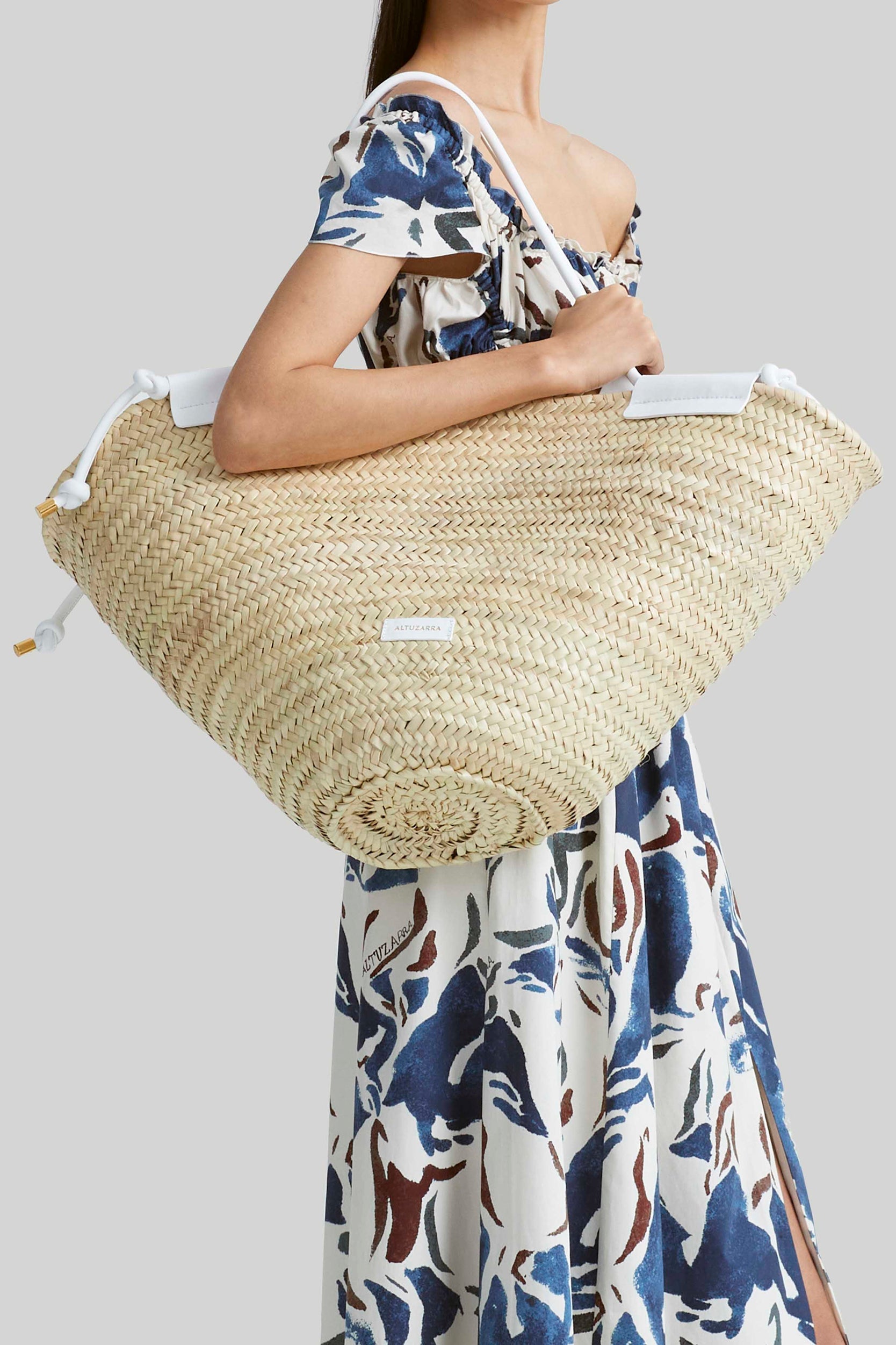 An individual holding an Altuzarra Basket Tote with leather straps, dressed in a floral-patterned dress.