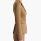 Clad in Altuzarra’s Fenice Jacket, this woman stands in profile against a white background, arms relaxed at her sides, effortlessly highlighting the impeccable suiting style of this tan virgin wool blend piece.