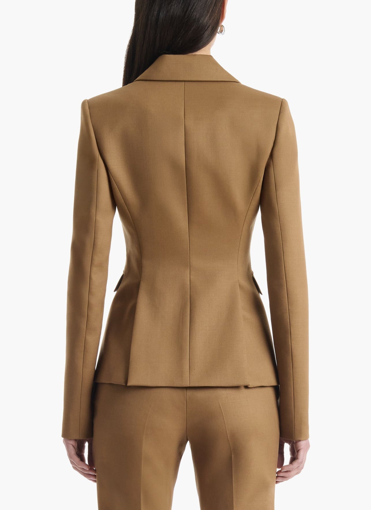 A person is photographed from the back against a plain white background, wearing a fitted tan Fenice Jacket by Altuzarra with matching virgin wool blend trousers, showcasing timeless classic suiting style.