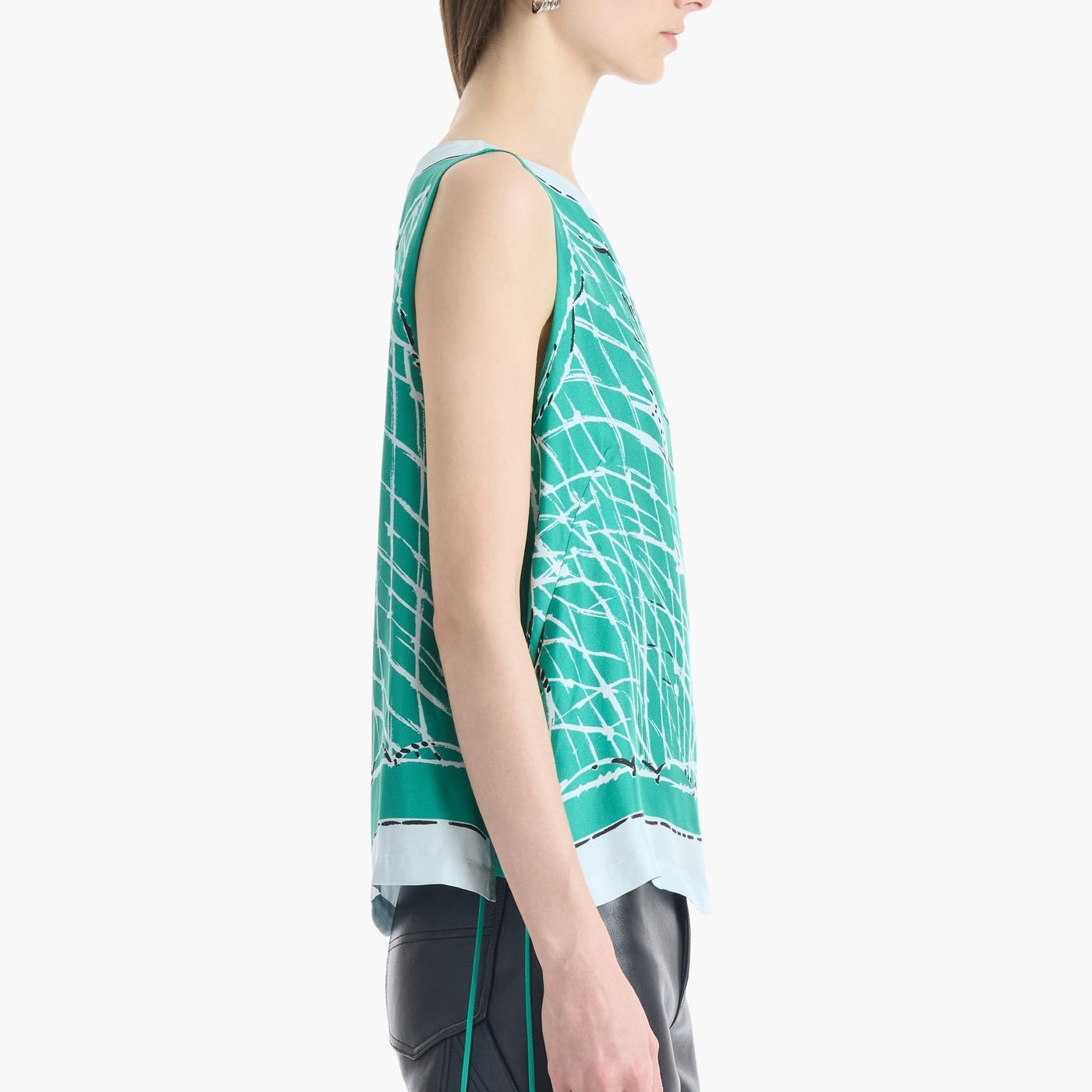 Model wearing the Altuzarra Siggi Top—a sleeveless green patterned silk piece with a wide neckline—paired with black pants, shown from the side against a plain white background.