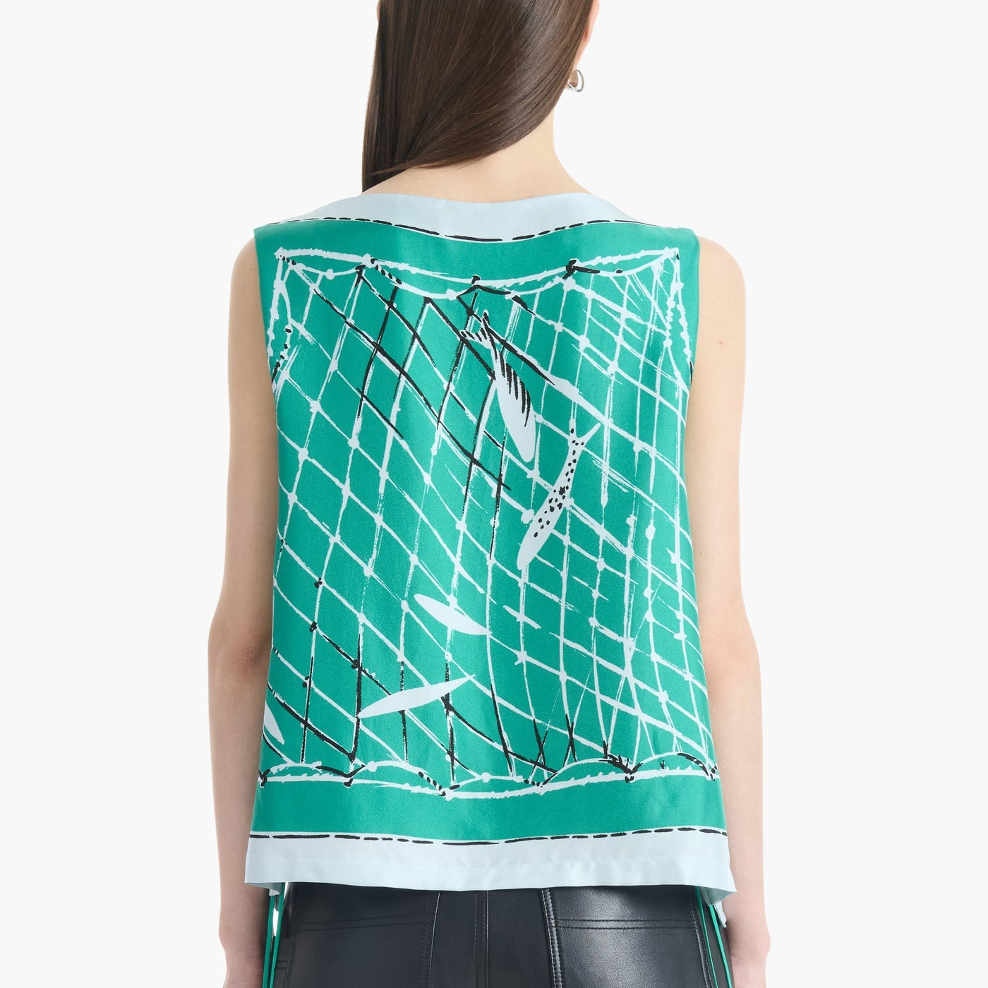 A person with straight brown hair wears the Altuzarra Siggi Top—a sleeveless green top featuring a white and black net pattern and a wide neckline—paired with black leather pants.