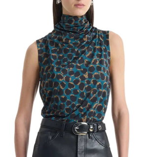 A woman wears the Altuzarra Holt Top, a relaxed sleeveless piece with a high draped neckline and teal and brown leopard print, styled with black belted leather pants for a straight silhouette.