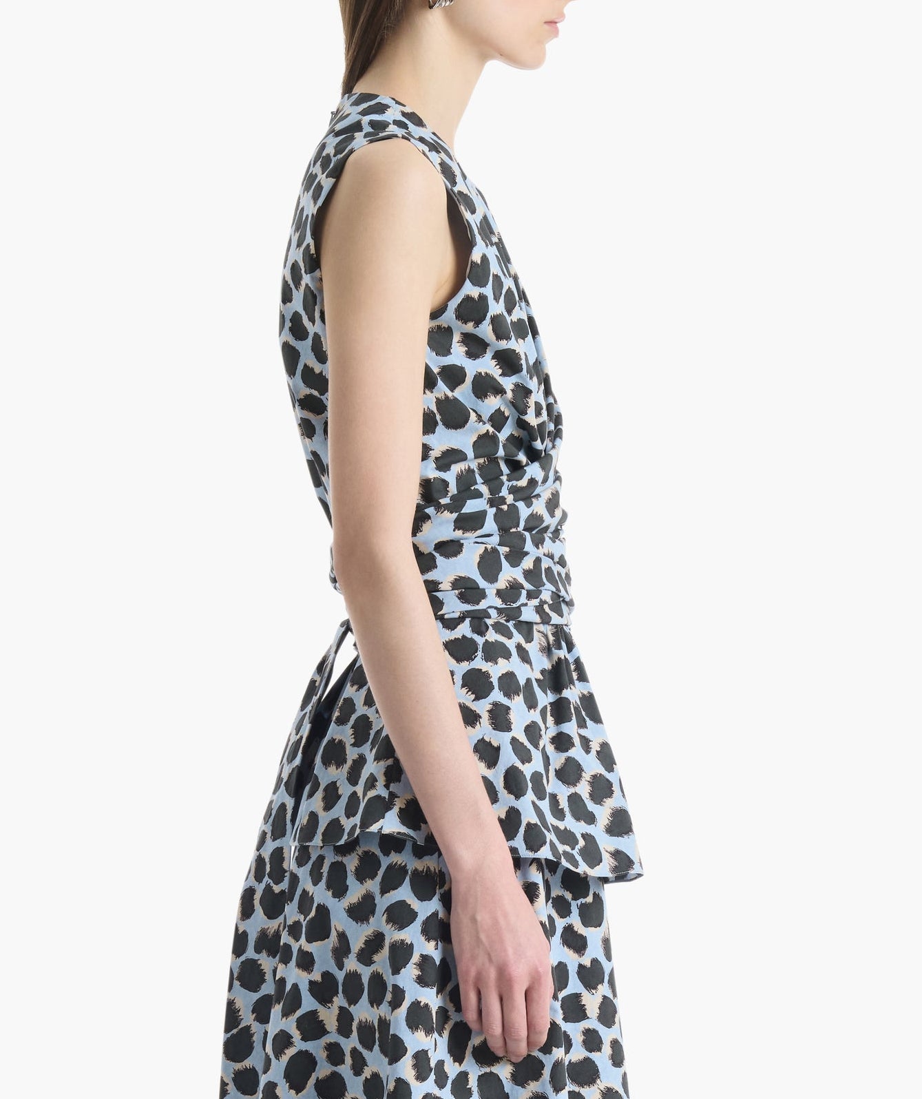 A woman wearing the Altuzarra Tizzy Top, a sleeveless blue and black leopard print style with a round neckline, is shown from the side against a plain white background.