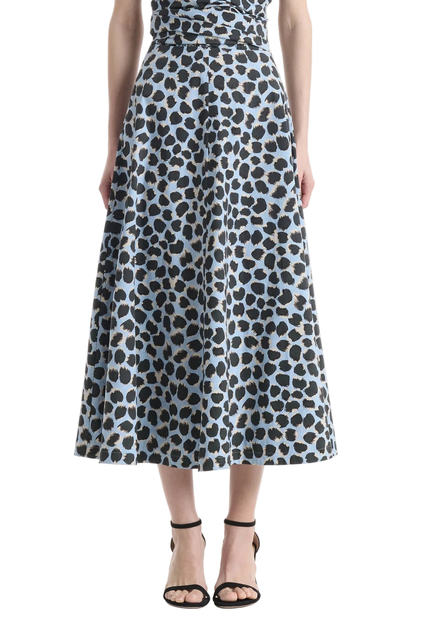 A woman showcasing the Altuzarra Varda Skirt—a high-waisted, A-line midi skirt featuring a blue and black leopard print crafted from soft cotton—pairs it with black strappy sandals for an effortlessly chic look.