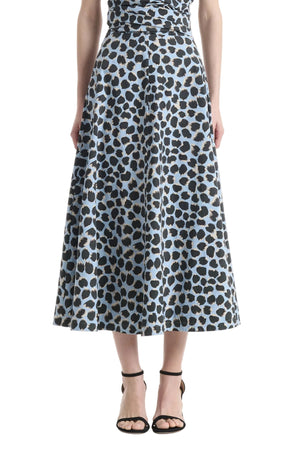 A woman showcasing the Altuzarra Varda Skirt—a high-waisted, A-line midi skirt featuring a blue and black leopard print crafted from soft cotton—pairs it with black strappy sandals for an effortlessly chic look.