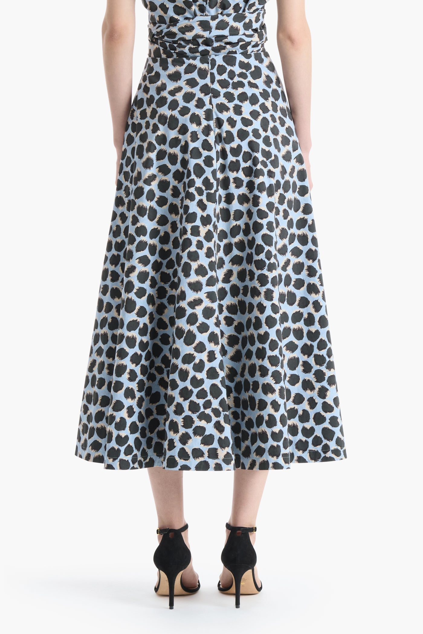 A person shown from the back against a white background wears the Altuzarra Varda Skirt, an A-line midi skirt in blue and black leopard print, paired with black high-heeled sandals.