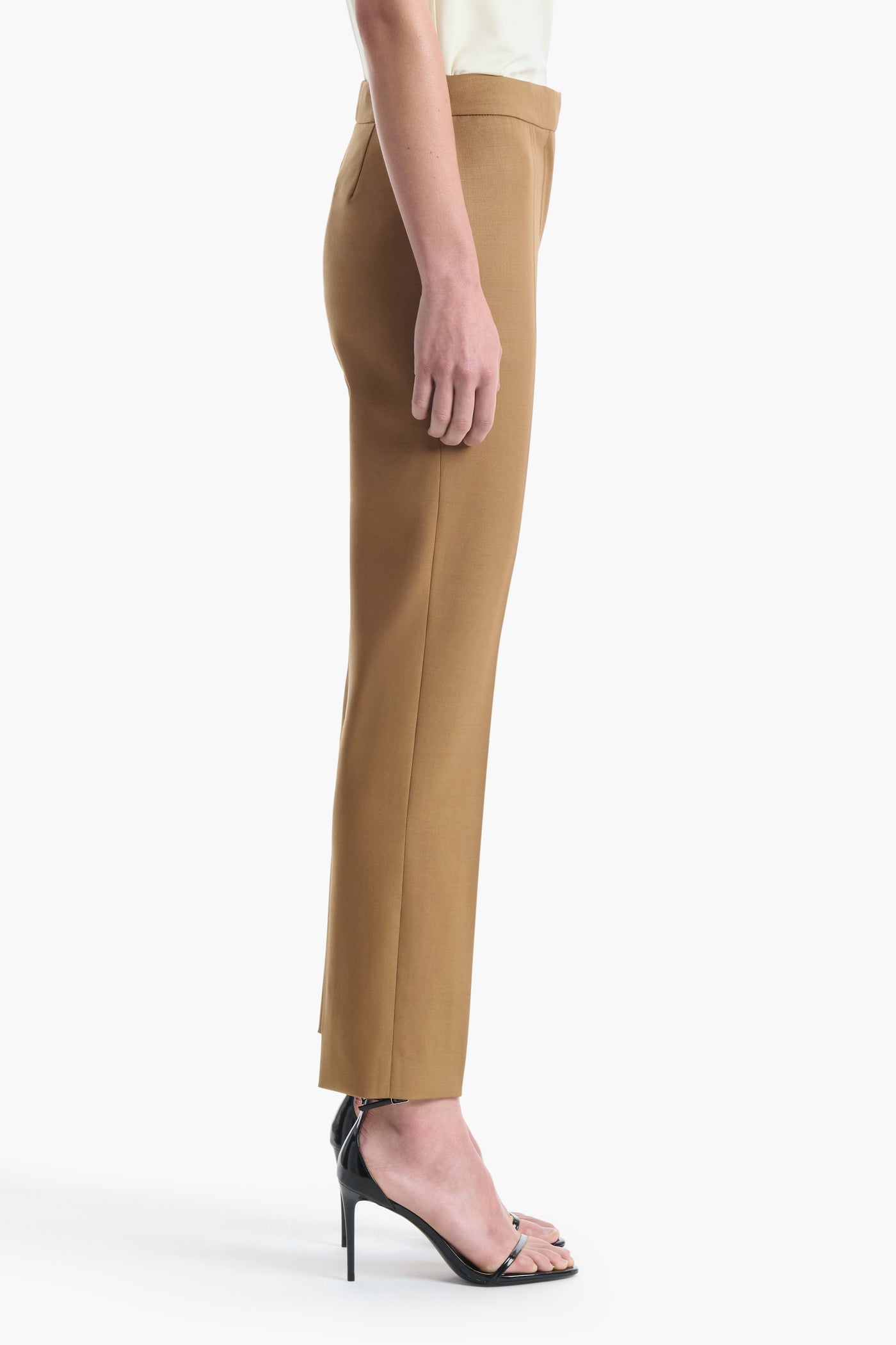 A person is shown in profile wearing the Altuzarra Todd Pant—tan tailored straight-leg pants—paired with black high-heeled sandals against a plain white background.