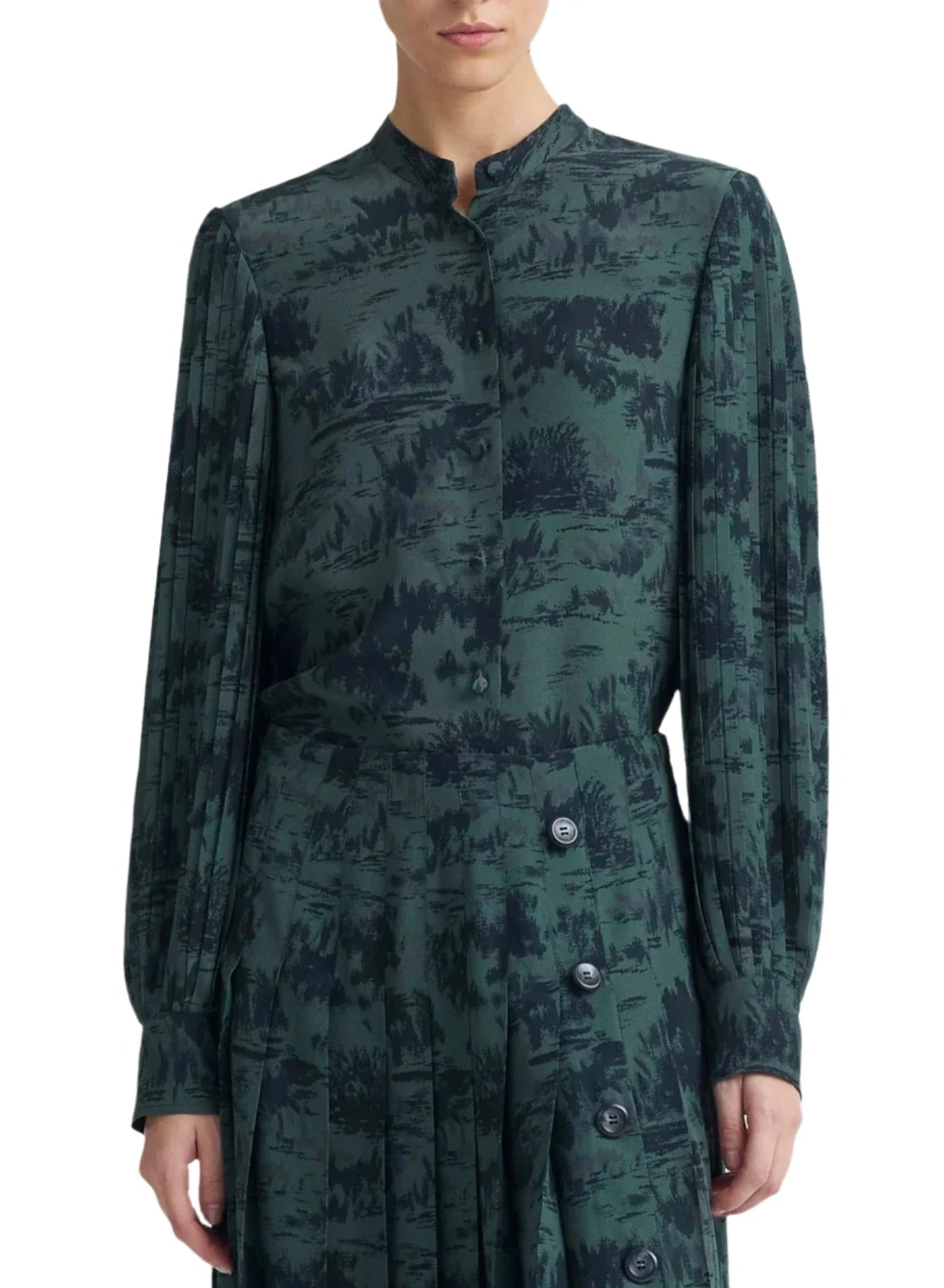 Person wearing a long-sleeved, dark green patterned Altuzarra Patsy Top with bishop sleeves and a matching skirt with large buttons on the side.