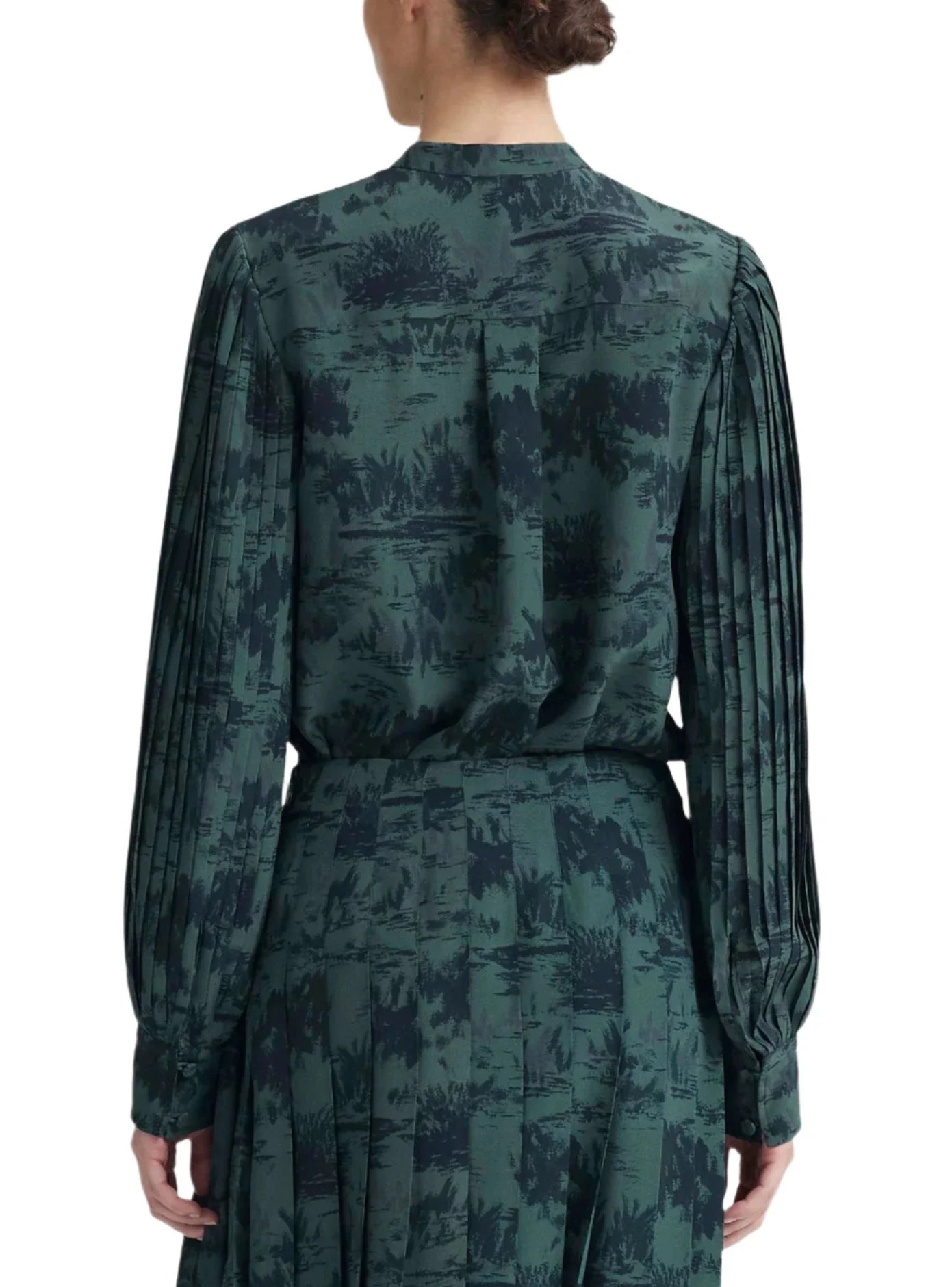 Rear view of a person with tied-back hair wearing a green, long-sleeved Altuzarra Patsy Top featuring pleated bishop sleeves and a nature-inspired pattern. The blouse, which includes a mandarin collar, is tucked into a matching skirt.