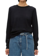 The person is wearing a 3.1 Phillip Lim Layered Knit Pullover with Keyhole in black, paired with blue jeans and a crisp white belt.