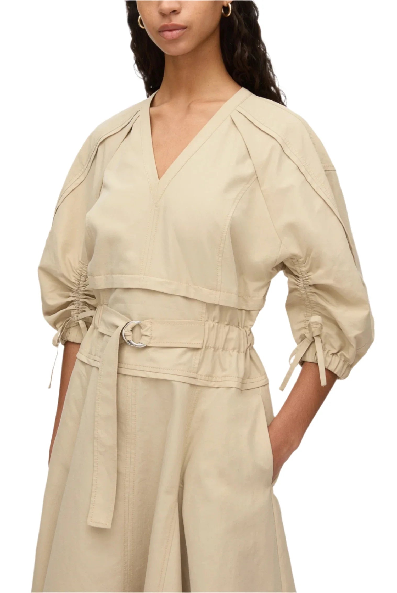 Someone is wearing the 3.1 Phillip Lim V Neck Dress with Gathered Sleeves, designed in beige Italian ottoman cotton. This dress highlights a cinched waist and belle sleeves, featuring a belt with a round buckle and convenient side pockets.