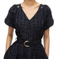 A person dressed in the 3.1 Phillip Lim Check Fil Coupe Tulip Dress, featuring a navy base with an irregular check motif, short sleeves, and stylish gold polished shoulder buttons, accessorized with a black belt adorned with a silver buckle.