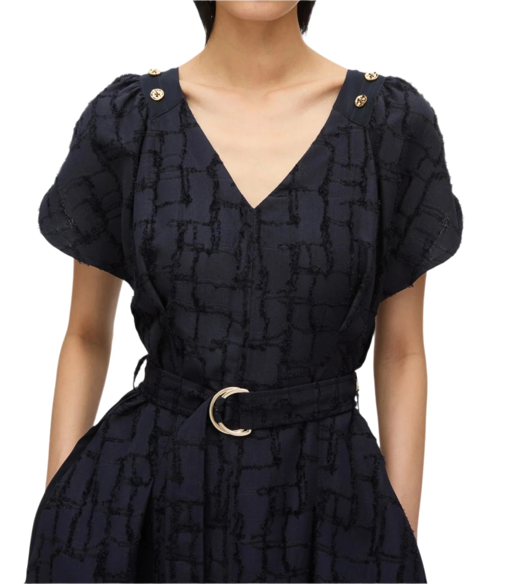 A person dressed in the 3.1 Phillip Lim Check Fil Coupe Tulip Dress, featuring a navy base with an irregular check motif, short sleeves, and stylish gold polished shoulder buttons, accessorized with a black belt adorned with a silver buckle.